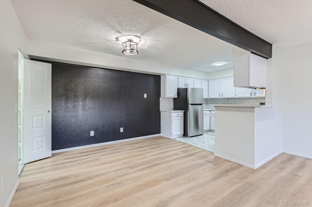 kitchen featuring tasteful backsplash, a textured ceiling, light hardwood / wood-style flooring, white cabinets, and stainless steel refrigerator