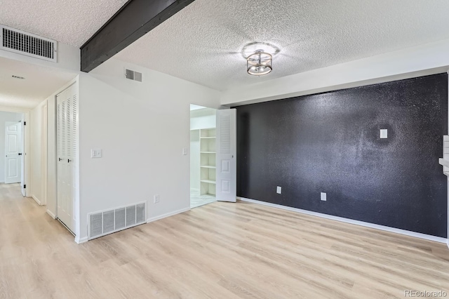 spare room with beam ceiling, light hardwood / wood-style floors, and a textured ceiling