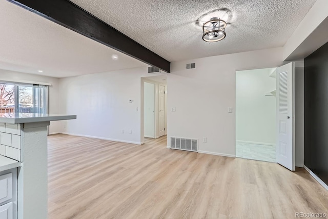 unfurnished living room with light hardwood / wood-style flooring, beamed ceiling, and a textured ceiling