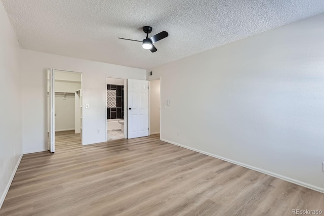 unfurnished bedroom featuring a textured ceiling, light hardwood / wood-style floors, a spacious closet, and ceiling fan