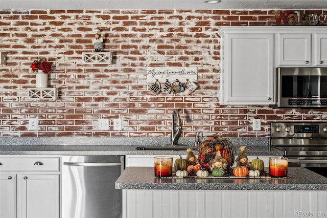 kitchen featuring a textured ceiling, white cabinetry, brick wall, sink, and stainless steel appliances