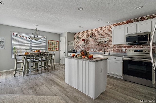 kitchen featuring stainless steel appliances, white cabinetry, brick wall, and a kitchen island