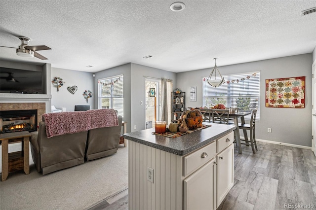 kitchen featuring pendant lighting, white cabinetry, a fireplace, a kitchen island, and light hardwood / wood-style floors