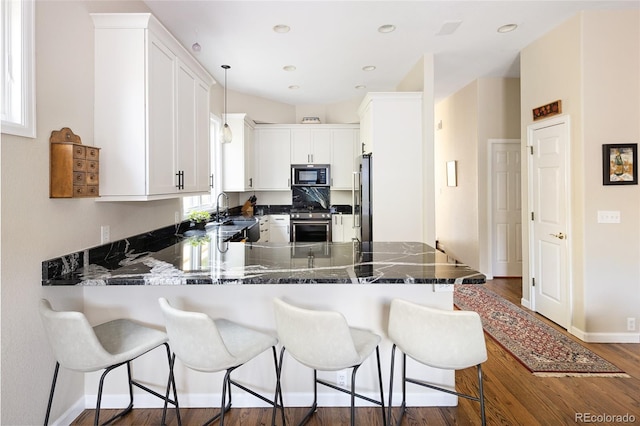 355 Steele St, Denver, CO 80206 - kitchen with stainless steel appliances, a peninsula, dark wood-style flooring, a breakfast bar area, and white cabinetry