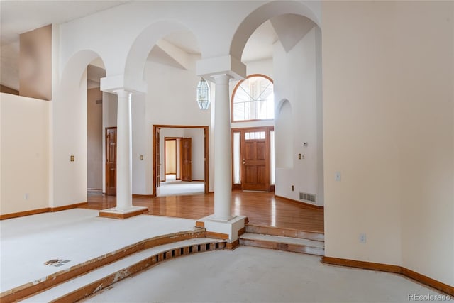 entryway with a towering ceiling, concrete flooring, and ornate columns