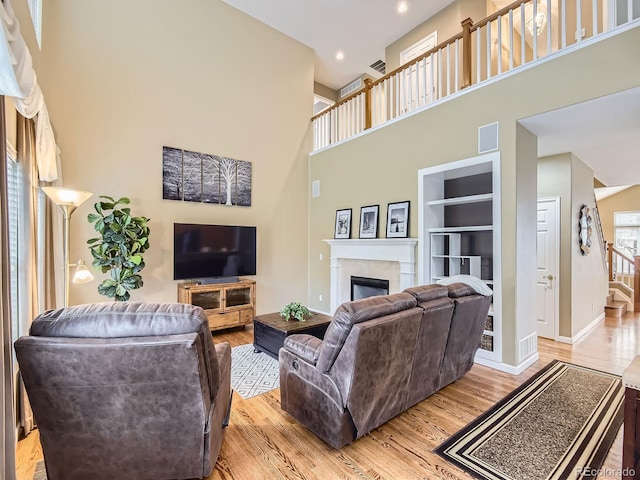 living room with a tiled fireplace, built in features, a high ceiling, and light hardwood / wood-style flooring