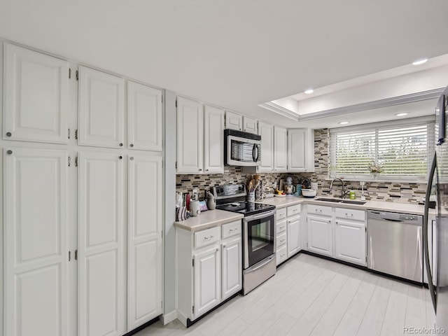 kitchen with appliances with stainless steel finishes, white cabinetry, tasteful backsplash, a raised ceiling, and sink