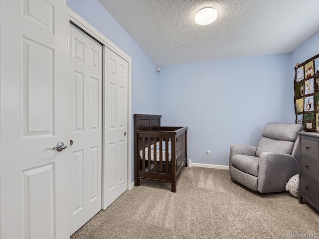 carpeted bedroom featuring a closet, a textured ceiling, and a crib