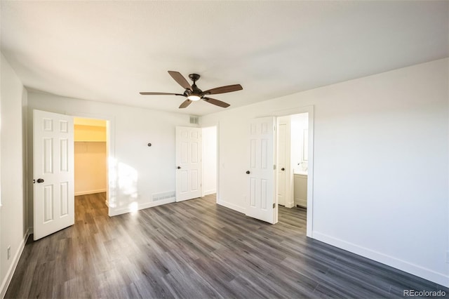 unfurnished bedroom featuring ensuite bath, a spacious closet, dark hardwood / wood-style floors, a closet, and ceiling fan