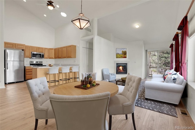 dining room featuring ceiling fan, light hardwood / wood-style floors, sink, and high vaulted ceiling