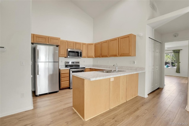 kitchen with high vaulted ceiling, sink, light hardwood / wood-style floors, kitchen peninsula, and stainless steel appliances