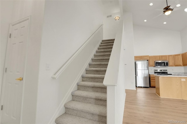 stairway featuring ceiling fan, wood-type flooring, and a high ceiling