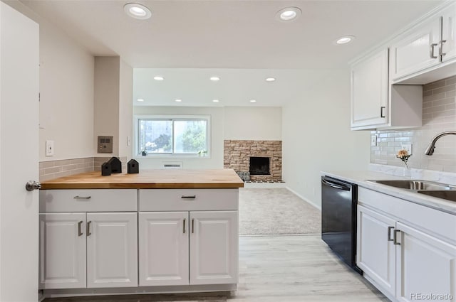 kitchen featuring a fireplace, black dishwasher, sink, white cabinets, and wooden counters