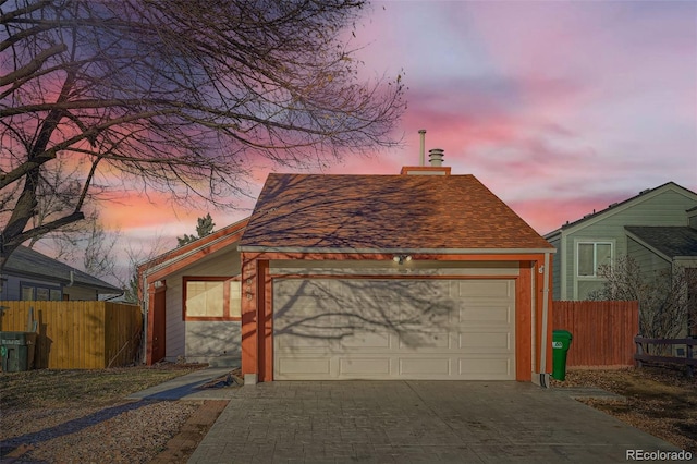 garage at dusk with concrete driveway and fence