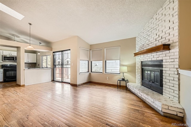 unfurnished living room with lofted ceiling with skylight, light wood finished floors, a textured ceiling, and a brick fireplace