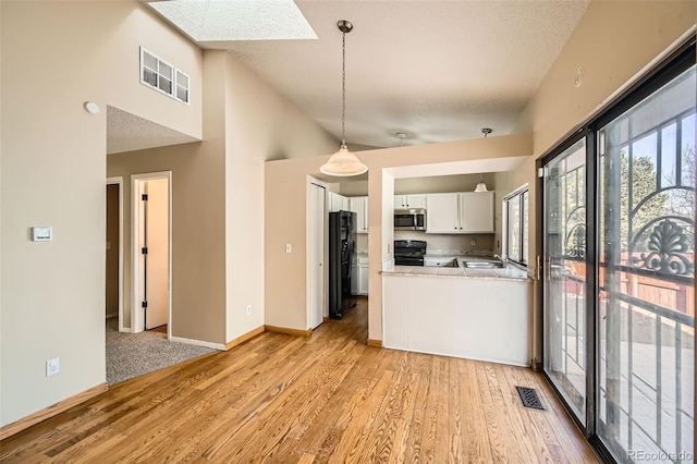 kitchen with visible vents, black appliances, a sink, white cabinets, and a skylight