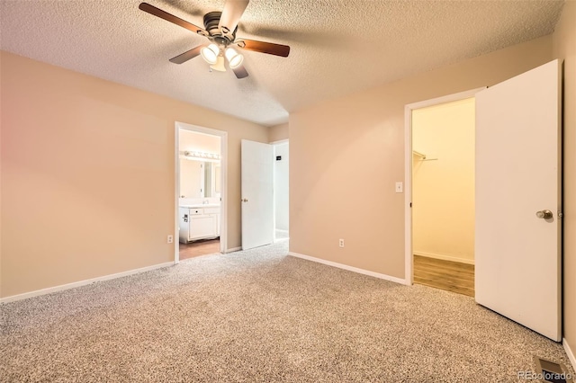 unfurnished bedroom with a spacious closet, baseboards, light carpet, ensuite bathroom, and a textured ceiling