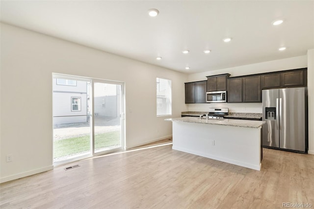 13467 Valentia St, Thornton, CO 80602 - kitchen featuring appliances with stainless steel finishes, light wood-type flooring, dark brown cabinets, an island with sink, and recessed lighting