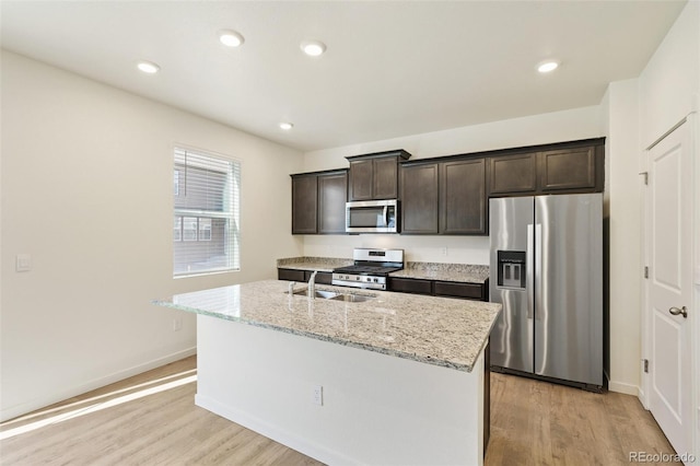 13467 Valentia St, Thornton, CO 80602 - kitchen with stainless steel appliances, light wood-style floors, dark brown cabinetry, an island with sink, and recessed lighting