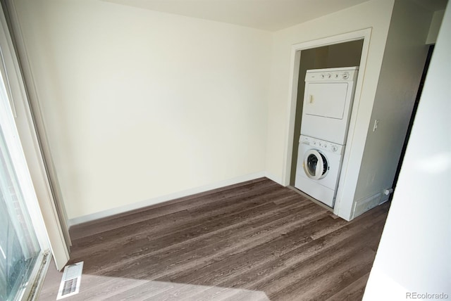 clothes washing area featuring stacked washer and dryer, laundry area, visible vents, baseboards, and dark wood-style flooring