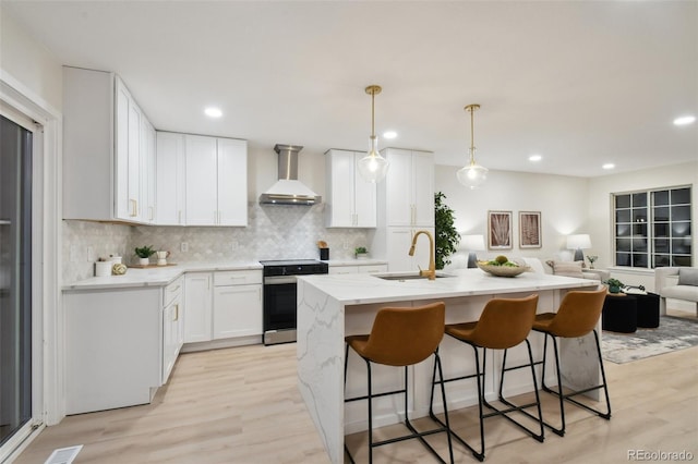 kitchen featuring wall chimney range hood, stainless steel range, sink, white cabinets, and light hardwood / wood-style floors