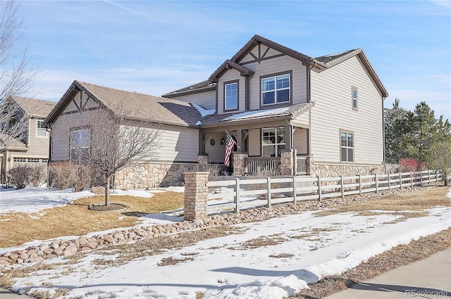 view of front of property with a fenced front yard, stone siding, and covered porch