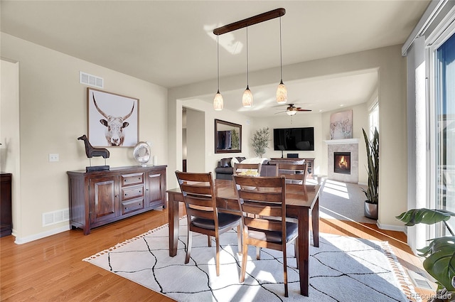 dining area with visible vents, light wood-style flooring, a warm lit fireplace, and baseboards