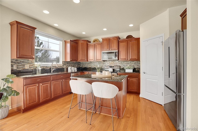 kitchen with light wood finished floors, a breakfast bar, a sink, appliances with stainless steel finishes, and a center island