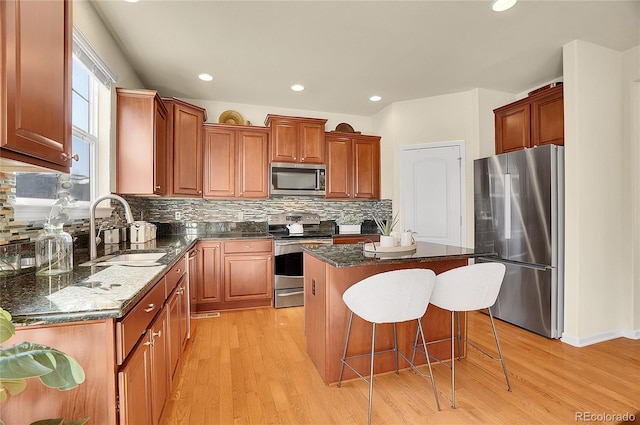 kitchen featuring a kitchen island, a kitchen breakfast bar, light wood-style floors, stainless steel appliances, and a sink