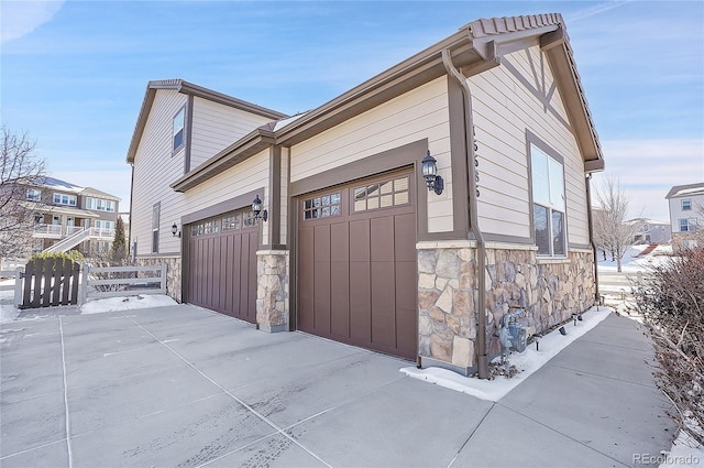 view of home's exterior with stone siding, driveway, a garage, and fence