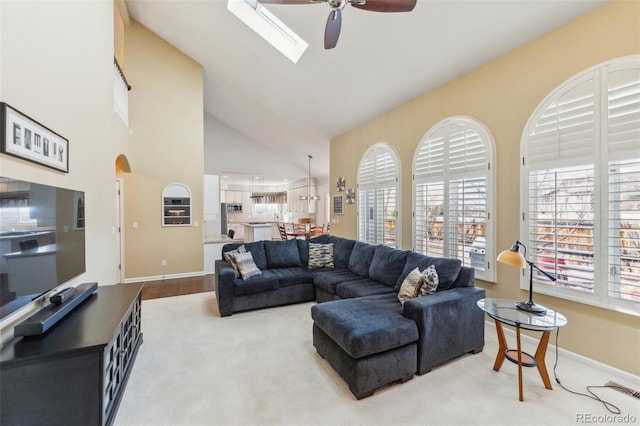 living area featuring baseboards, high vaulted ceiling, a skylight, and ceiling fan