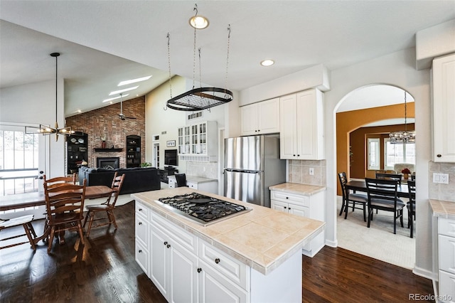 kitchen with dark wood finished floors, stainless steel appliances, vaulted ceiling, ceiling fan with notable chandelier, and a large fireplace