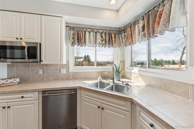 kitchen with tasteful backsplash, appliances with stainless steel finishes, white cabinetry, and a sink