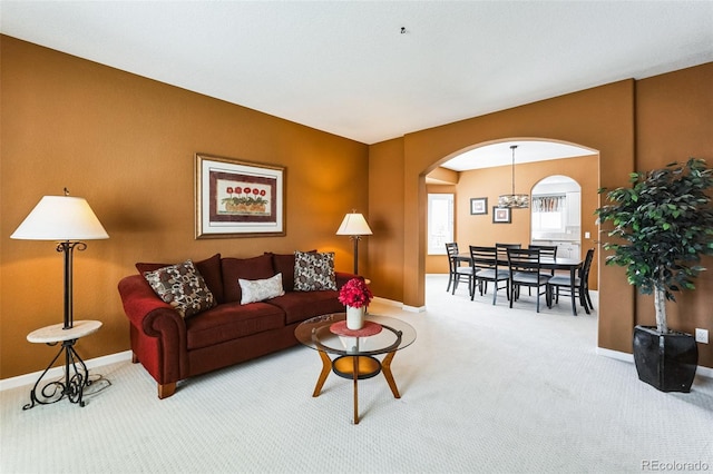 carpeted living area with arched walkways, an inviting chandelier, and baseboards