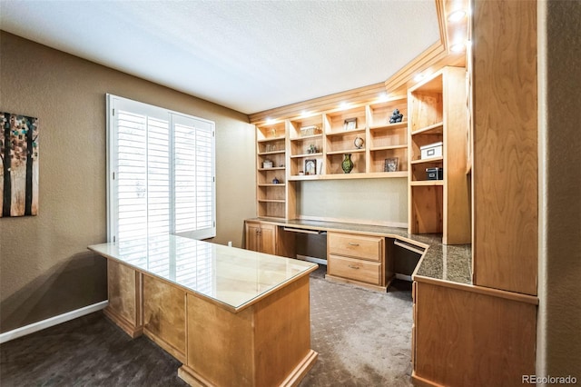 office with a textured wall, built in desk, dark colored carpet, and a textured ceiling