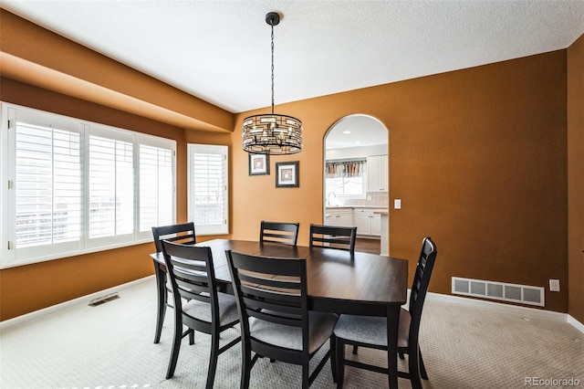 carpeted dining space featuring arched walkways, visible vents, and baseboards