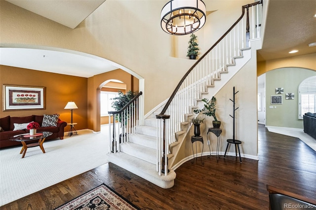 staircase with plenty of natural light, wood finished floors, arched walkways, and baseboards