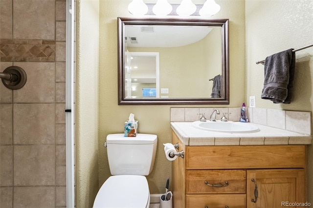 bathroom with vanity, toilet, visible vents, and a tile shower