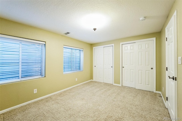 unfurnished bedroom featuring a textured ceiling, visible vents, two closets, and carpet floors