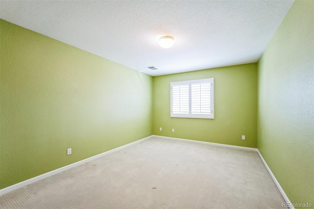 spare room featuring visible vents, baseboards, light colored carpet, and a textured ceiling