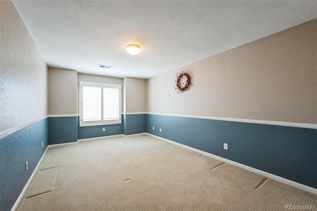 carpeted empty room with visible vents, a textured wall, baseboards, and a textured ceiling