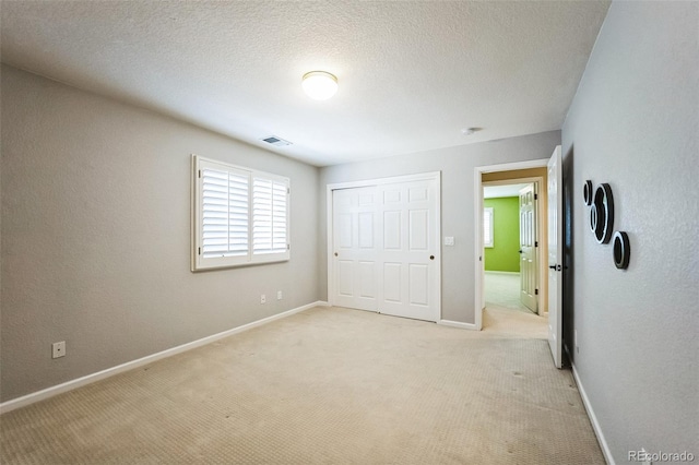 unfurnished bedroom with visible vents, baseboards, light carpet, a closet, and a textured ceiling