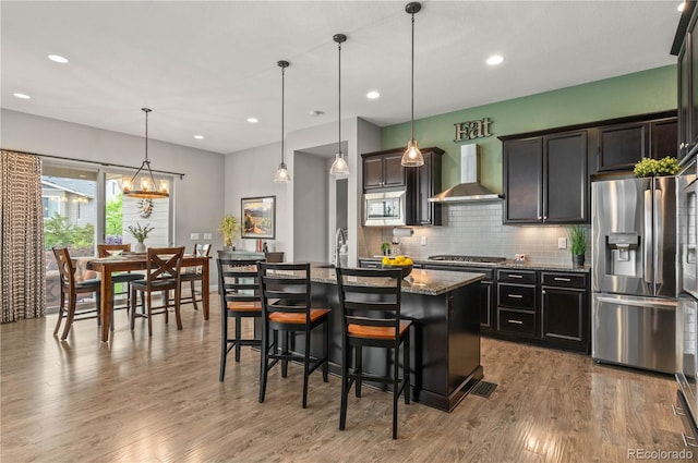 17358 W 95th Ave, Arvada, CO 80007 - kitchen with appliances with stainless steel finishes, wall chimney range hood, dark stone countertops, a kitchen island, and wood finished floors