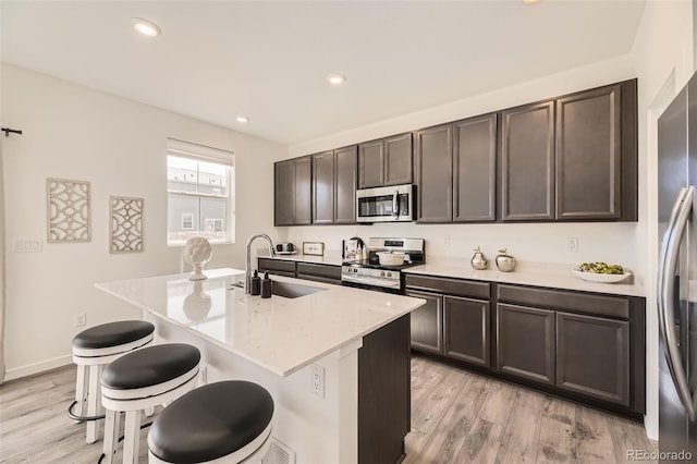 kitchen featuring appliances with stainless steel finishes, a breakfast bar, a sink, and light wood-style flooring