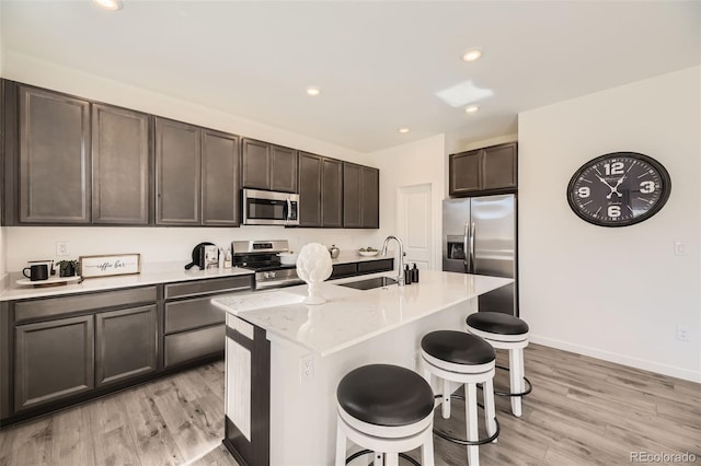 kitchen featuring stainless steel appliances, light wood finished floors, a kitchen bar, and a sink