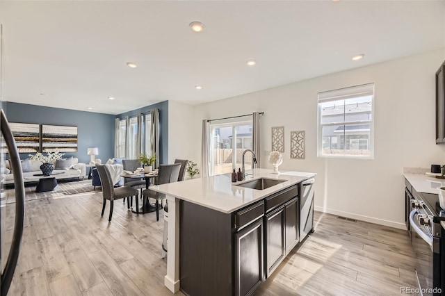 kitchen with light wood finished floors, stainless steel electric range oven, light countertops, and a sink