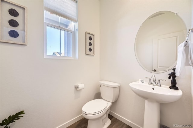 half bathroom featuring wood finished floors, toilet, and baseboards