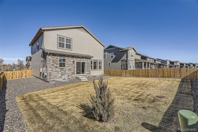 back of property with entry steps, stone siding, a fenced backyard, and a lawn