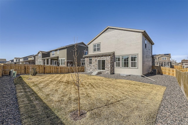 rear view of house with stone siding, a yard, cooling unit, and a fenced backyard