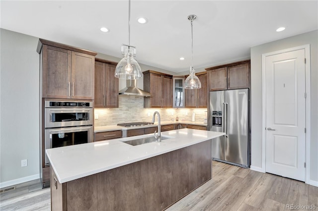 kitchen with wall chimney range hood, stainless steel appliances, light wood-style flooring, and a sink